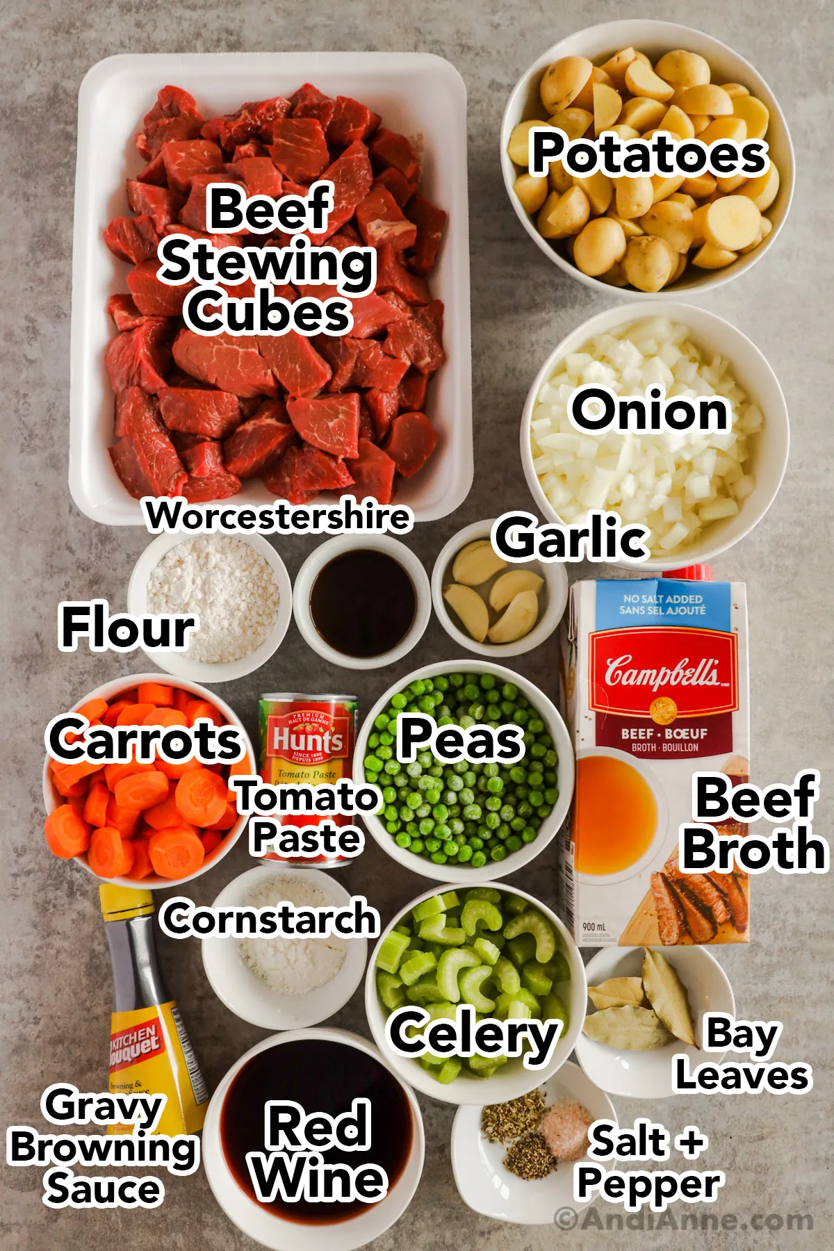 Overhead view of all the ingredients in bowls on the table. Beef cubes, potatoes, onion, Worcestershire, garlic, flour, carrots, tomato paste, peas, beef broth, cornstarch celery, bay leaves, salt, pepper, red wine, and gravy browning sauce. 
