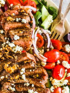 Sliced medium rare steak in a steak salad topped with crumbled blue cheese.
