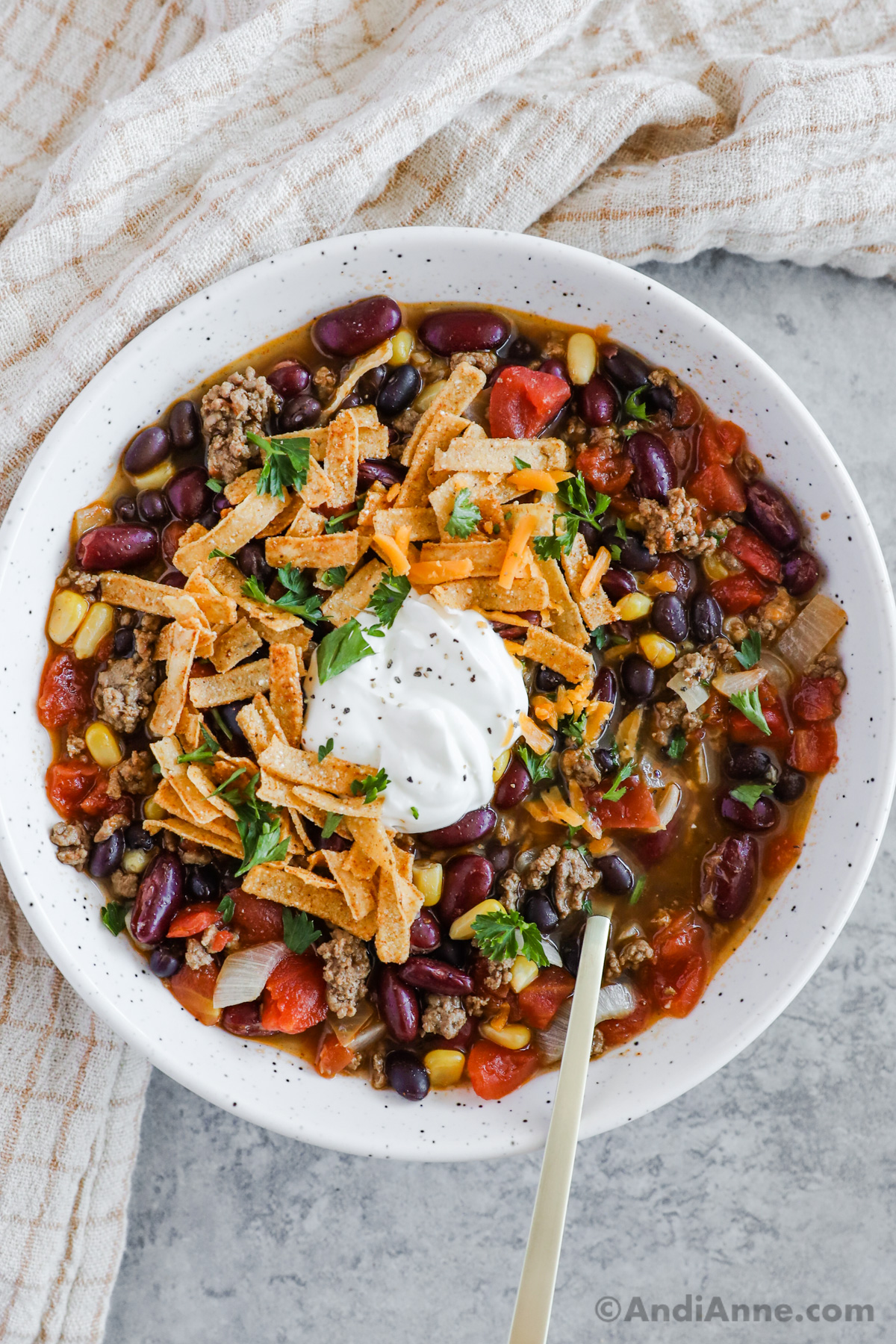 A plate with ground beef taco soup topped with tortilla crisps and dollop of sour cream.