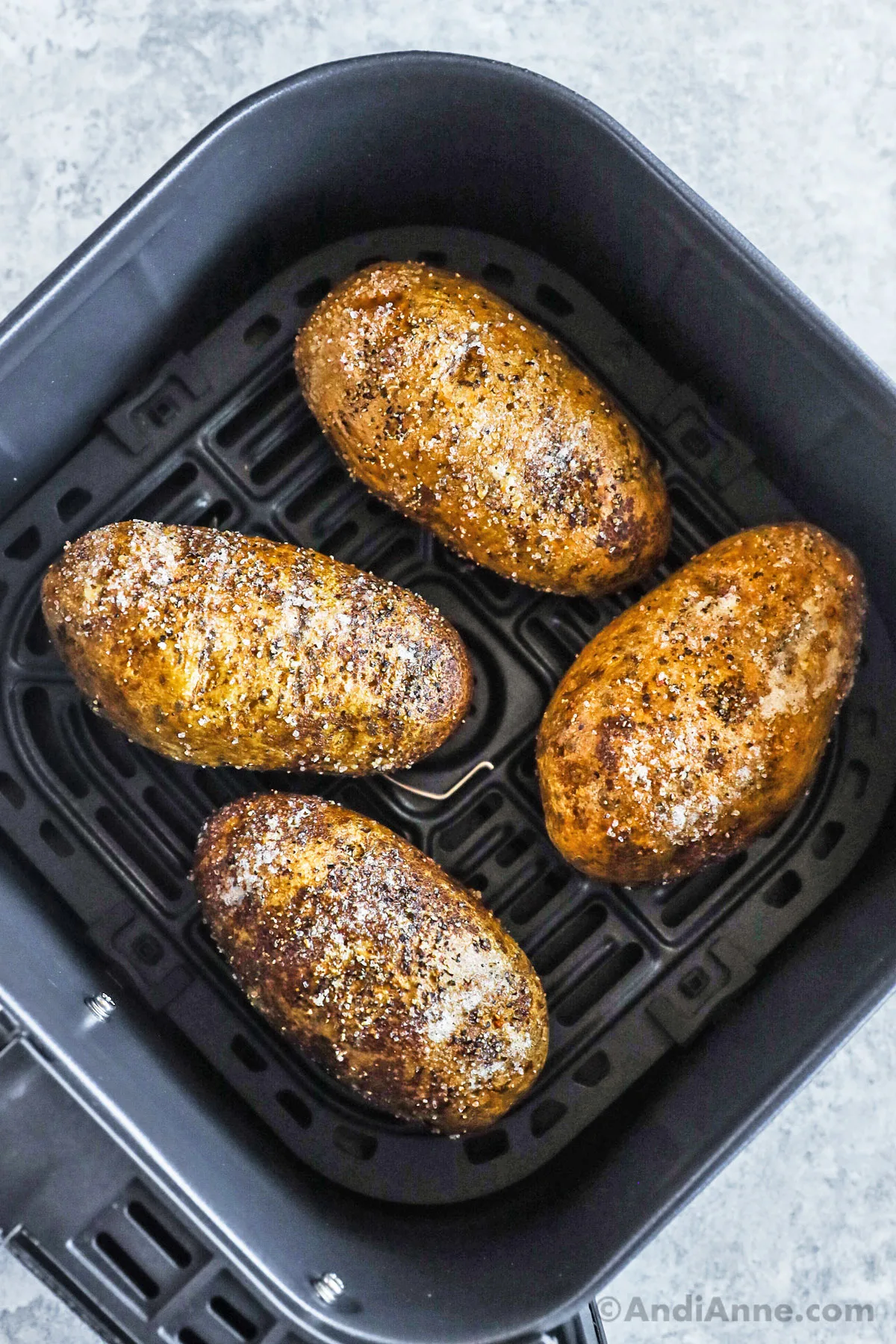 An air fryer basket with baked russet potatoes inside.
