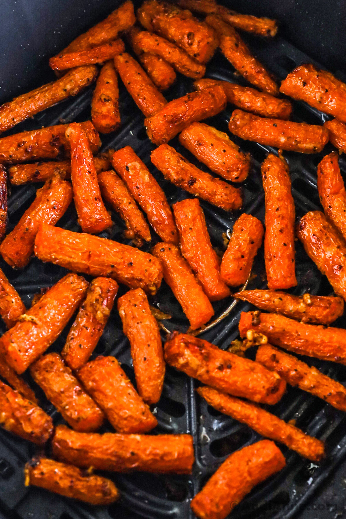 Close up of an air fryer basket with cooked carrots inside,