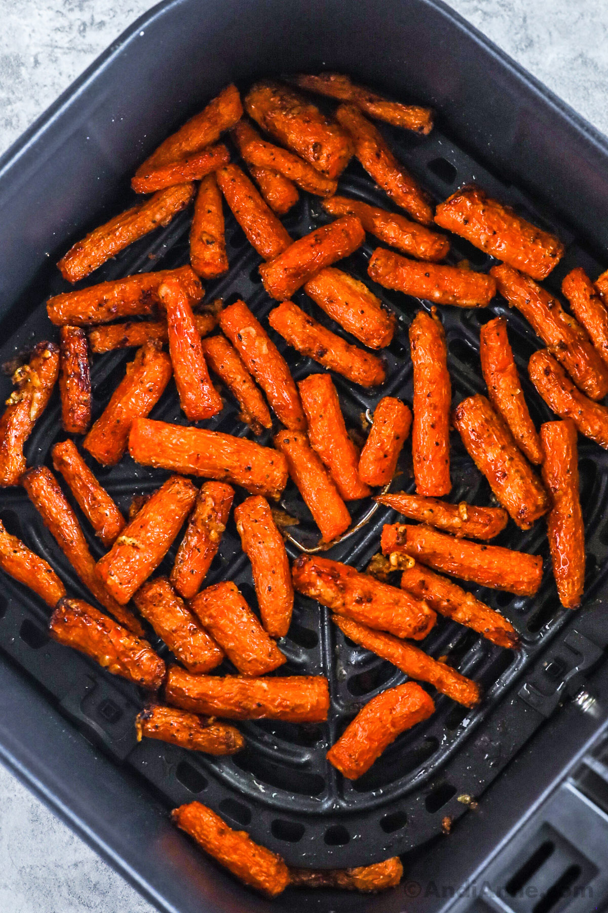 An air fryer basket with cooked carrots inside.