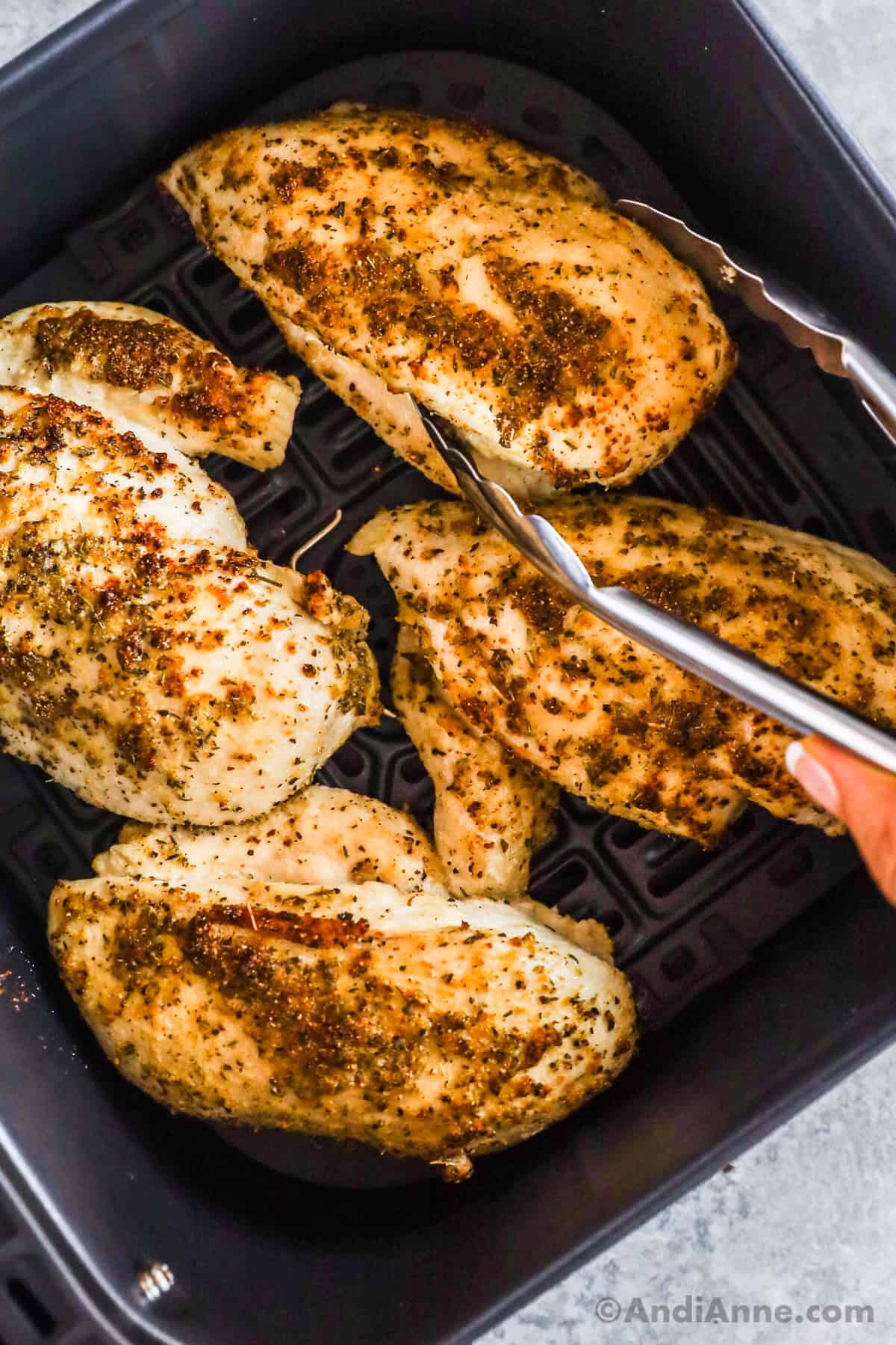 Chicken breasts in an air fryer with tongs over one piece