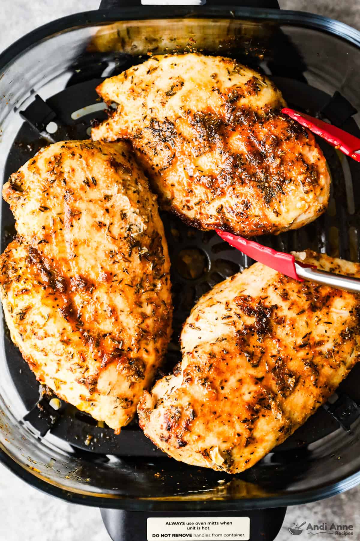chicken breasts in an air fryer with tongs