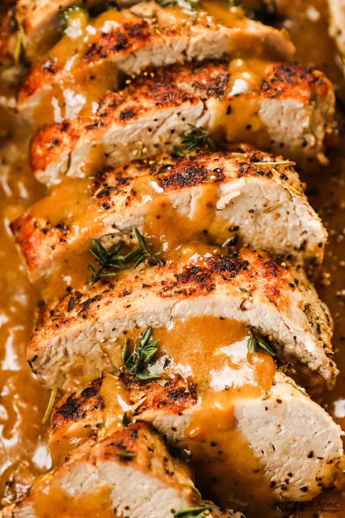 A close-up of sliced pork tenderloin with pan gravy drizzled over top.