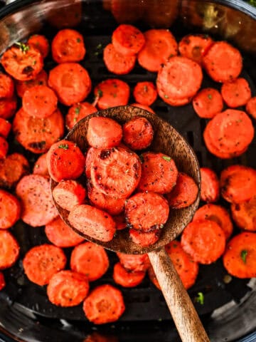 close up of cooked carrots on a wood spoon above an air fryer