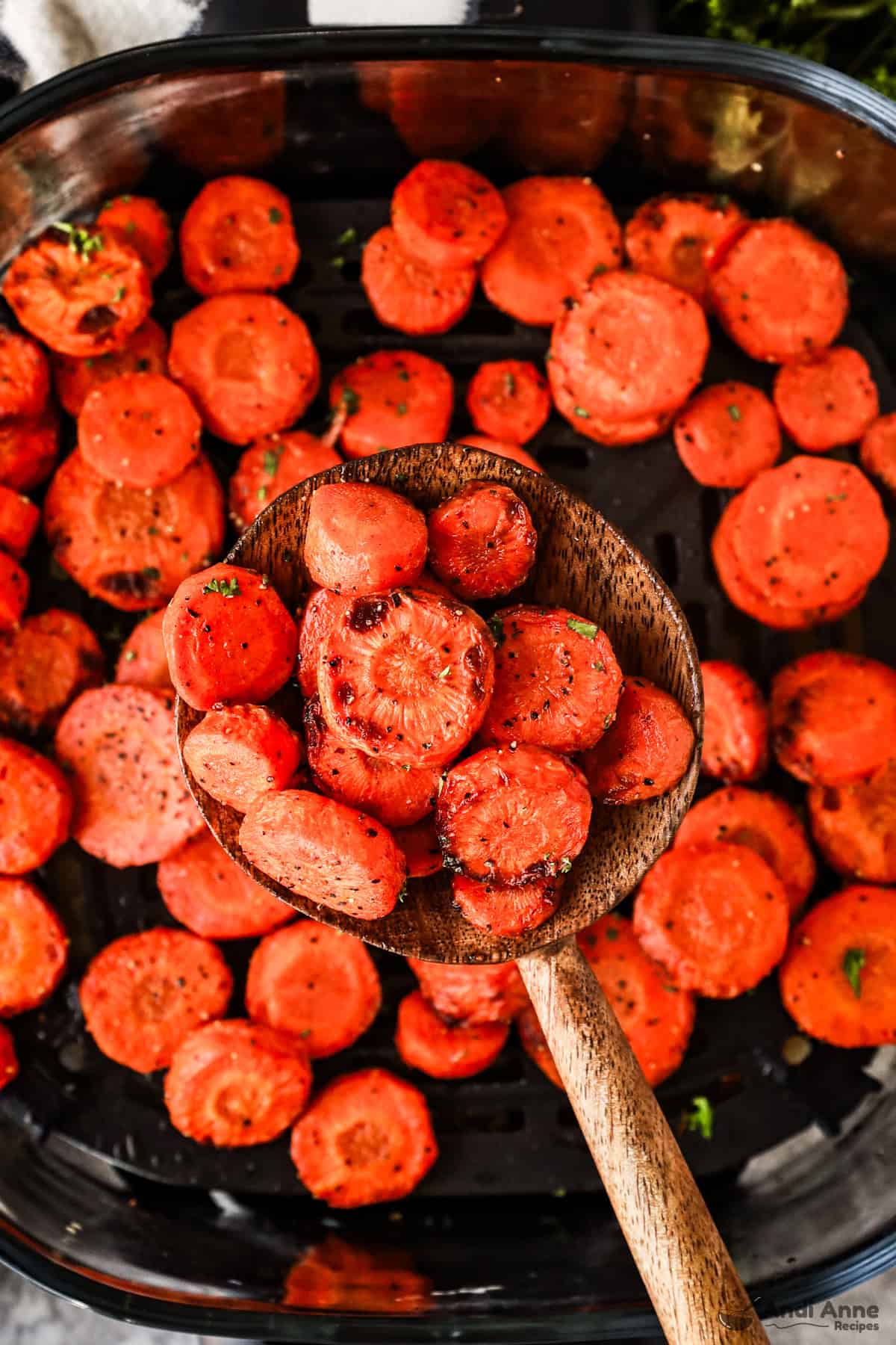 close up of cooked carrots on a wood spoon above an air fryer