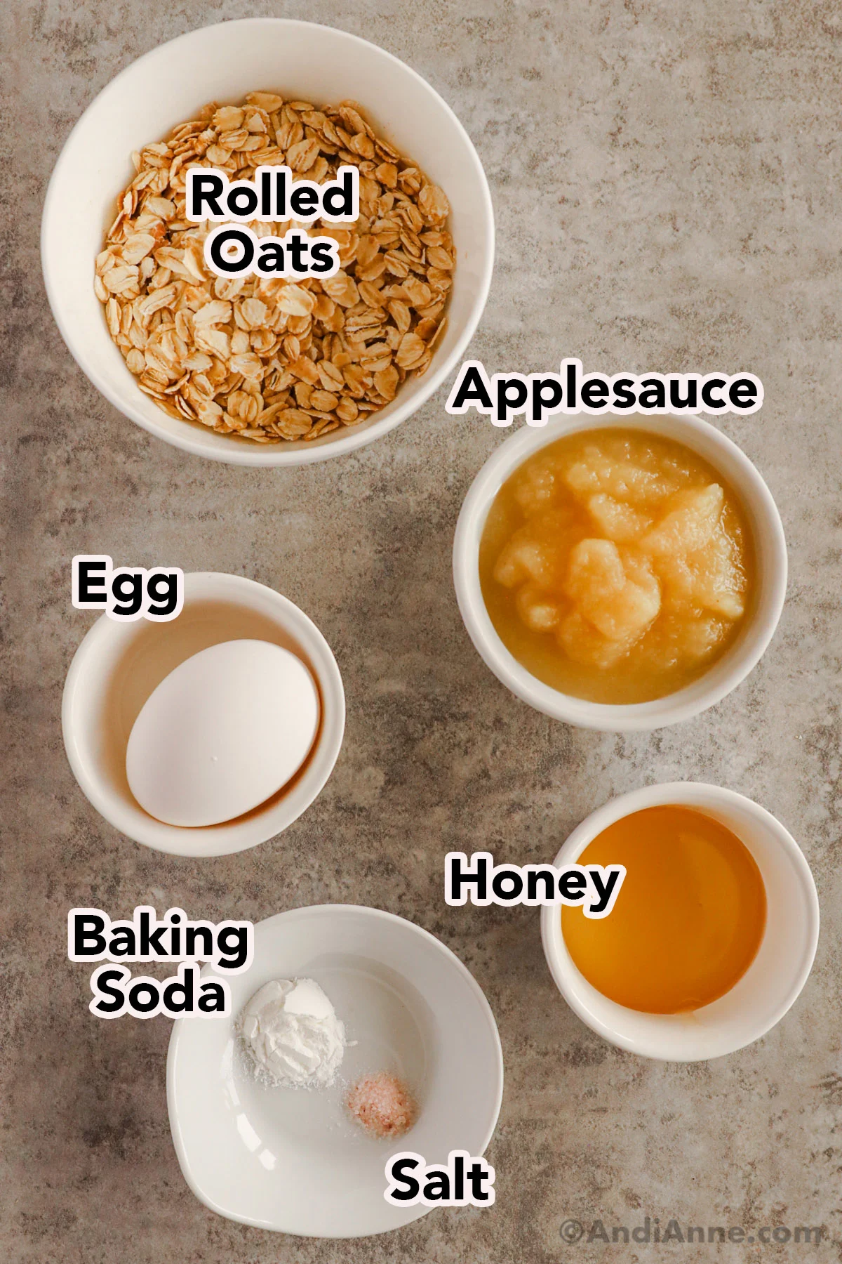 Recipe ingredients in bowls including rolled oats, applesauce, egg, baking soda and honey.