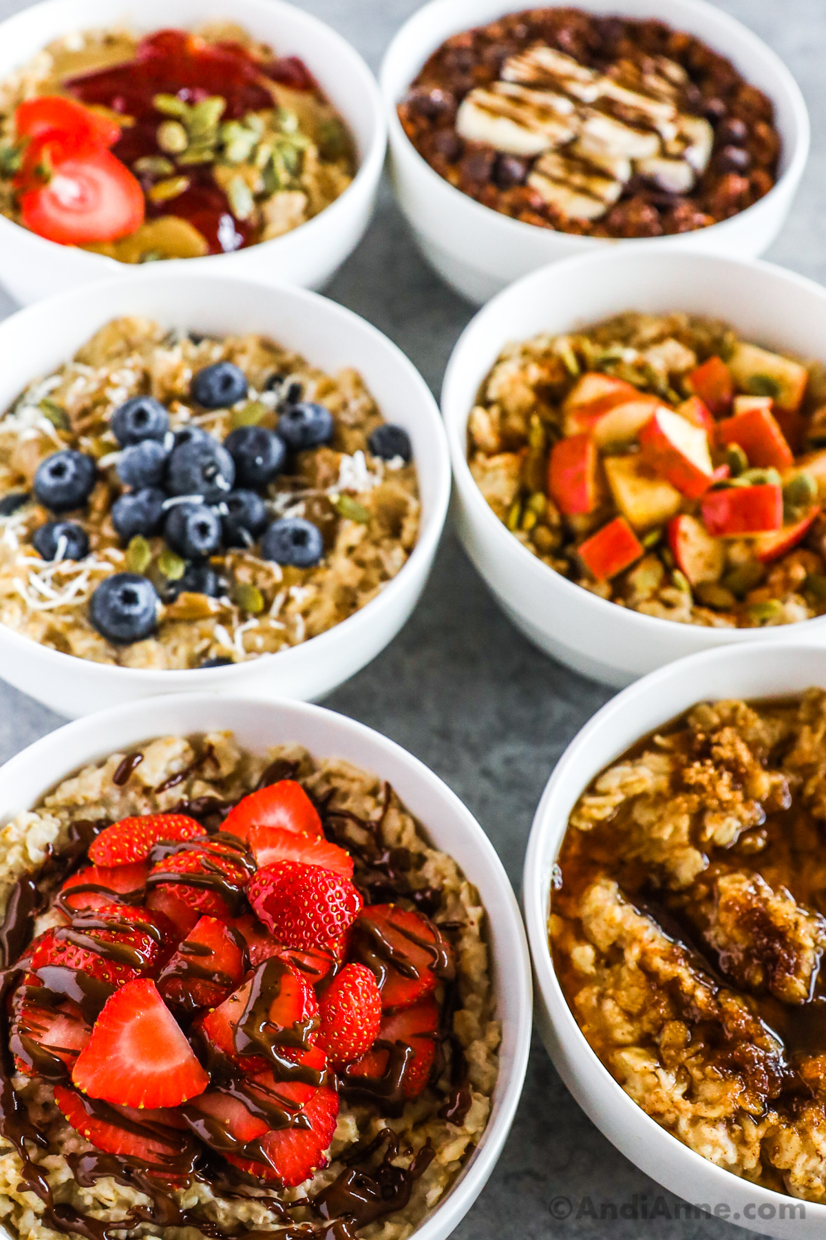 Close up of bowls of oatmeal flavors including strawberry drizzle with nutella, blueberries, chopped apple, chocolate with banana, peanut butter and jam.