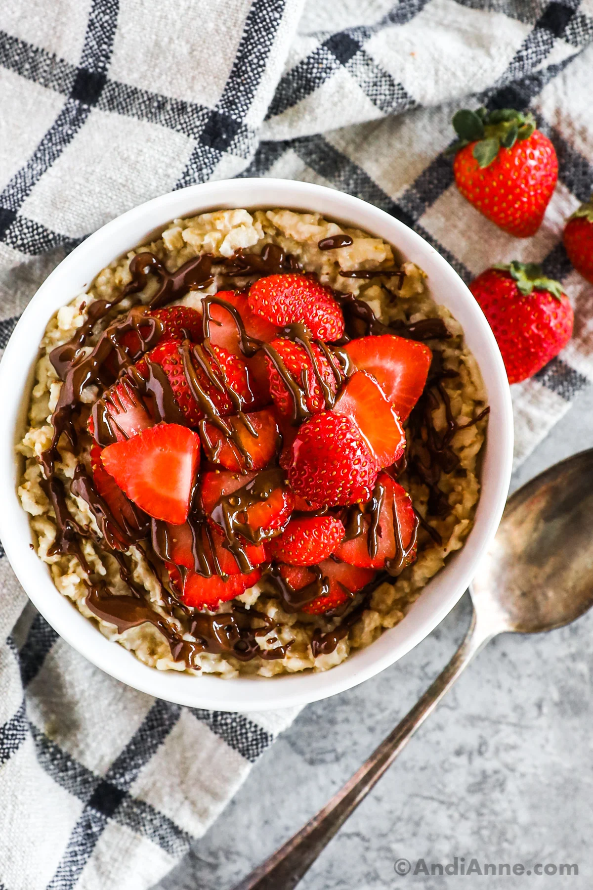 Bowl of strawberry oatmeal topped with sliced strawberries and drizzled with nutella.