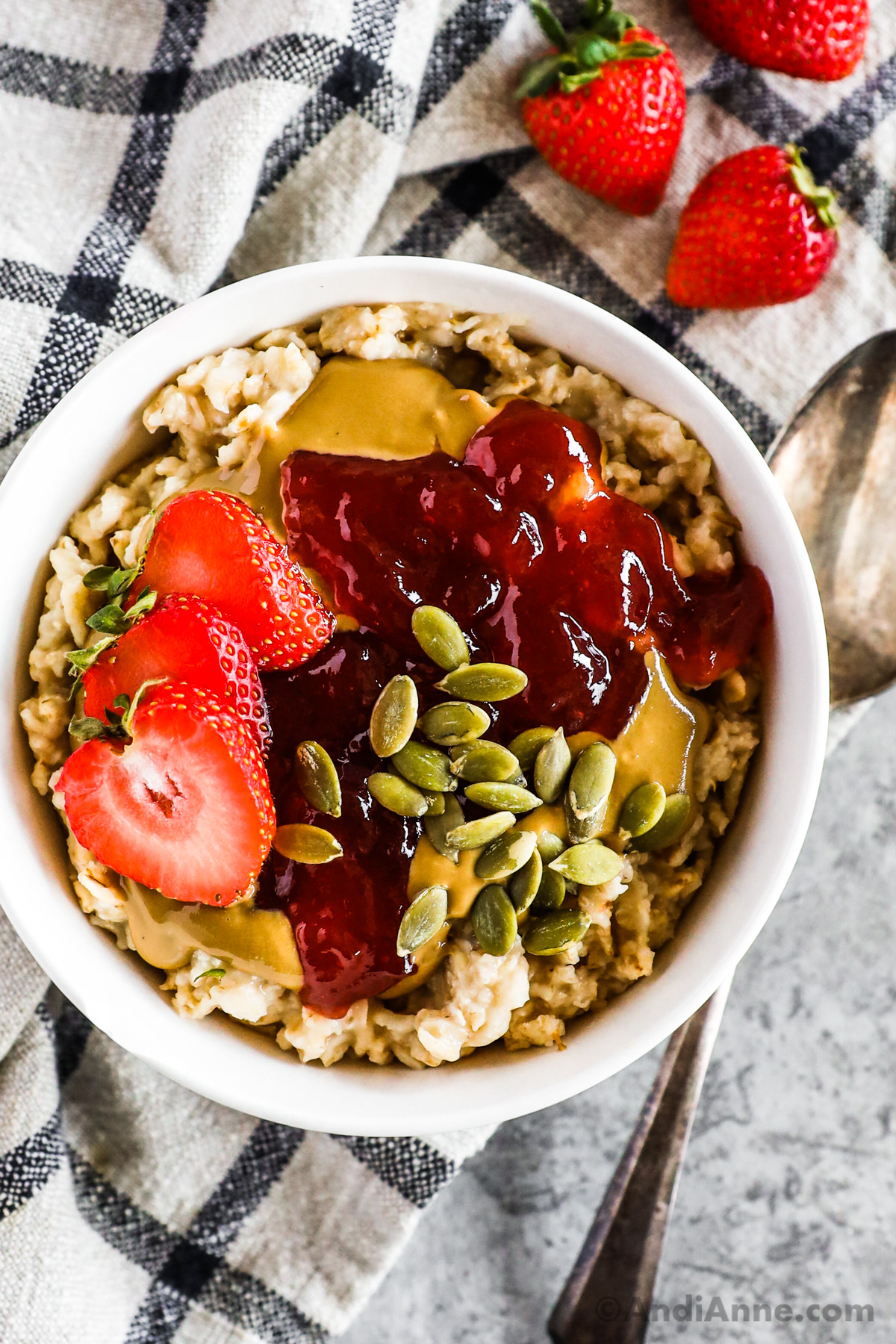 Bowl of peanut butter and jam oatmeal with pumpkin seeds and sliced strawberries.