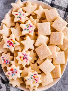 A plate of butter cookies in various cut out shapes. Some topped with sprinkles.