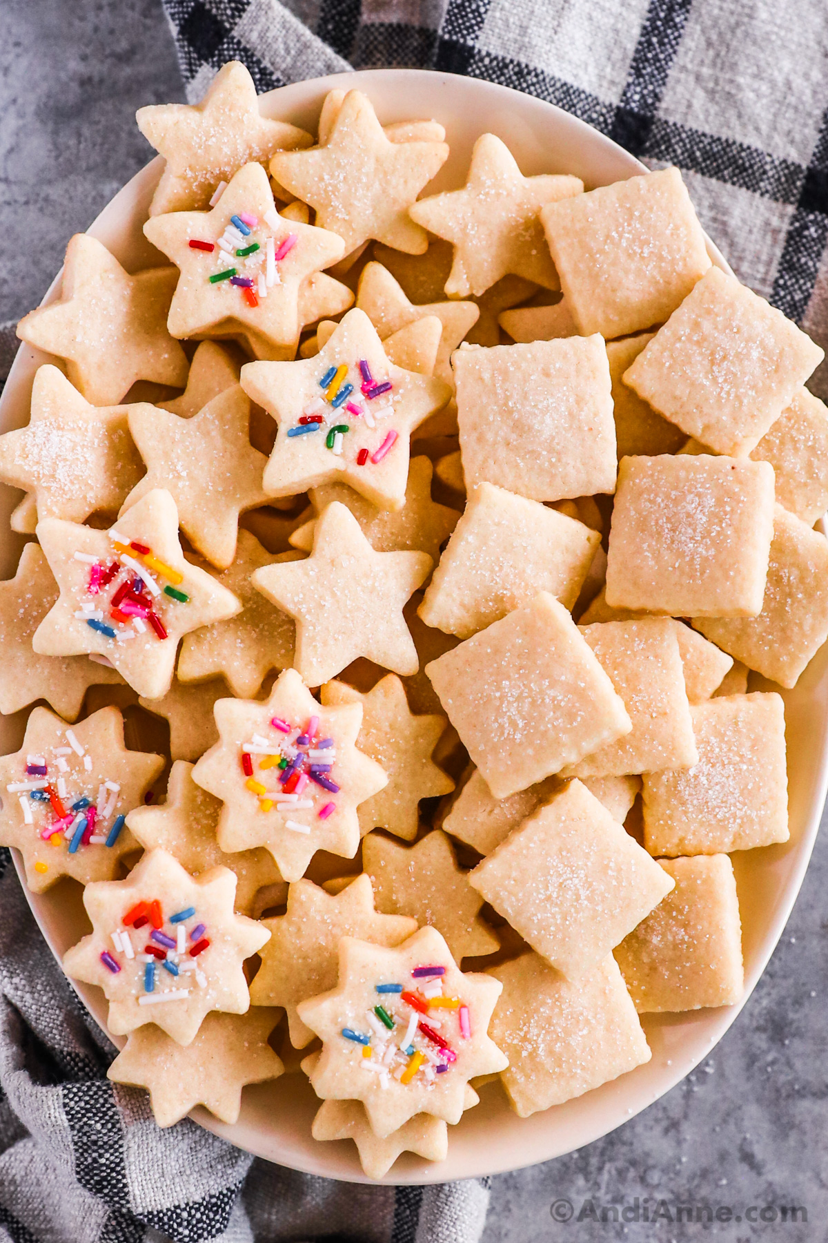 A plate of butter cookies in different cut out shapes lightly sprinkled with sugar, some with sprinkles