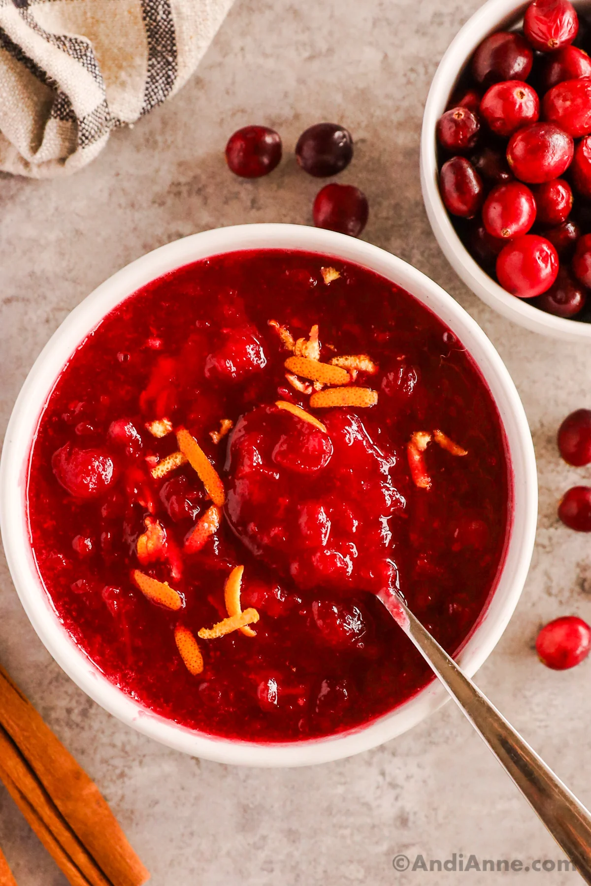 Close up of bowl of cranberry sauce with a spoon and orange zest on top. 