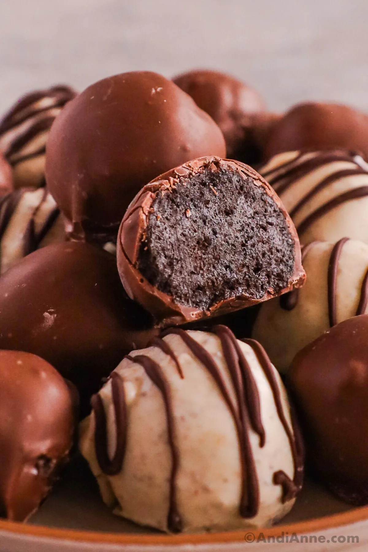 Close up of white and milk chocolate balls. Some drizzled with milk chocolate over top. One is sliced open to see the inside of the oreo ball.