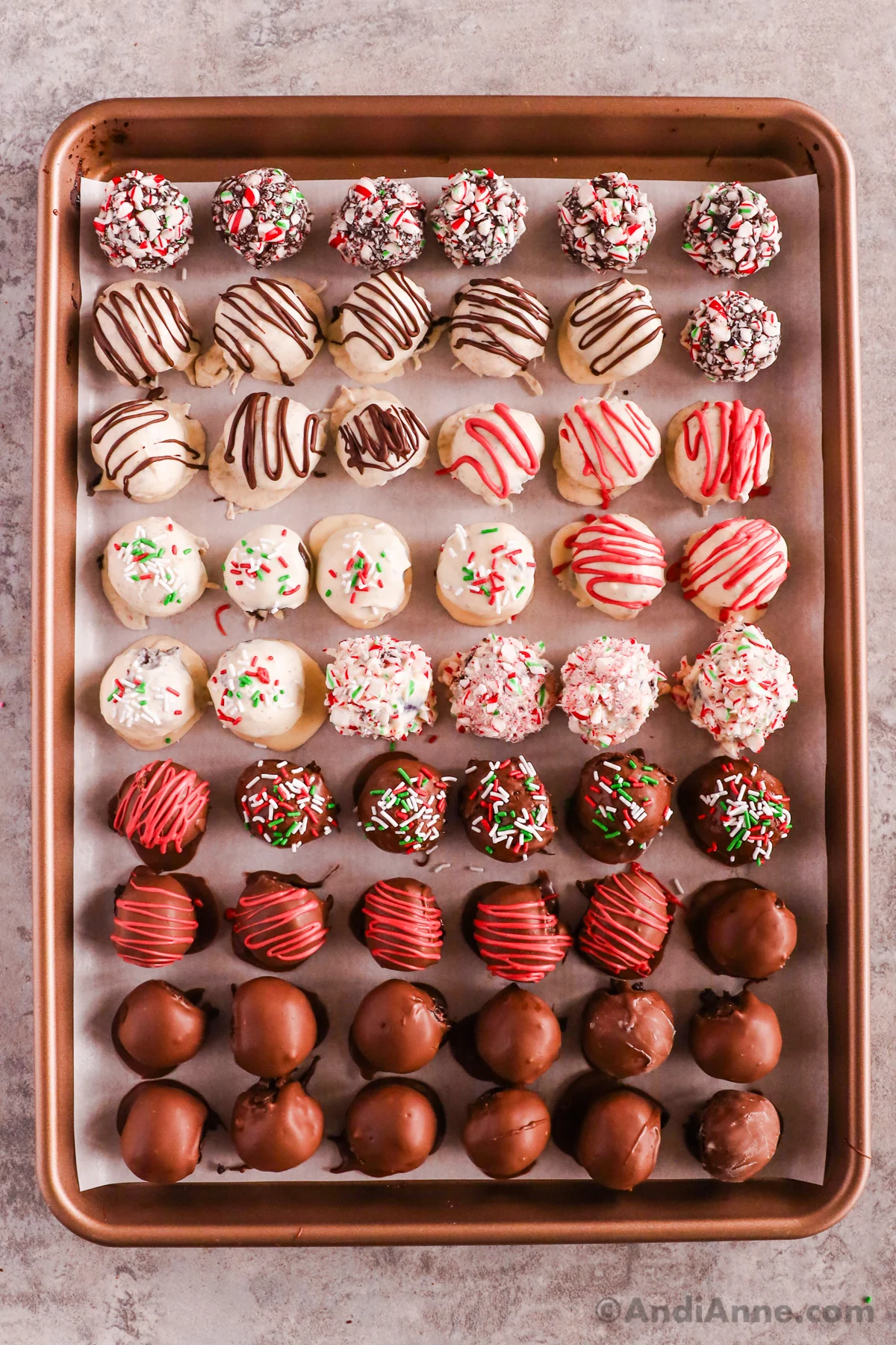 A baking sheet with lots of oreo balls with various decorations. Either dipped in white or milk chocolate. Some with sprinkles, crushed candy canes, drizzled with chocolate or red candy melts. 