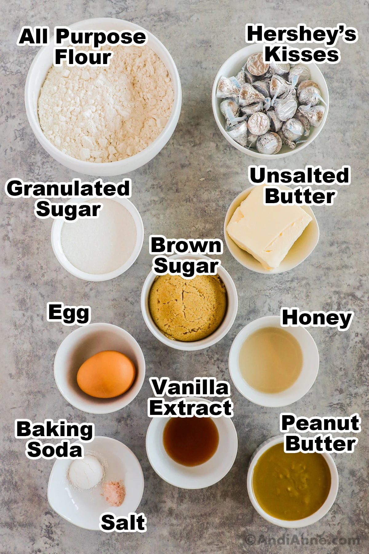Recipe ingredients in bowls including flour, hersheys kisses, sugar, butter, eggs, brown sugar, honey, baking soda, vanilla nad peanut butter.