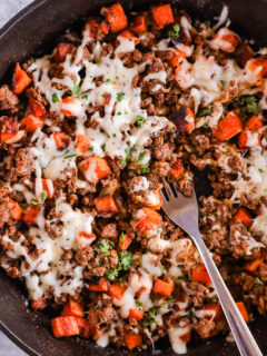 A skillet with ground beef sweet potato dinner topped with melted cheese