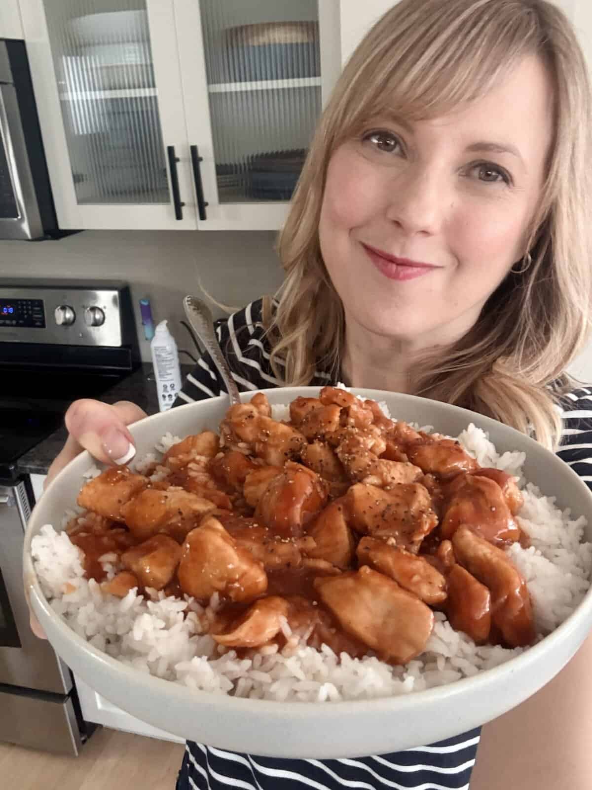 Andi is holding a plate of sweet and sour chicken on a bed of rice.