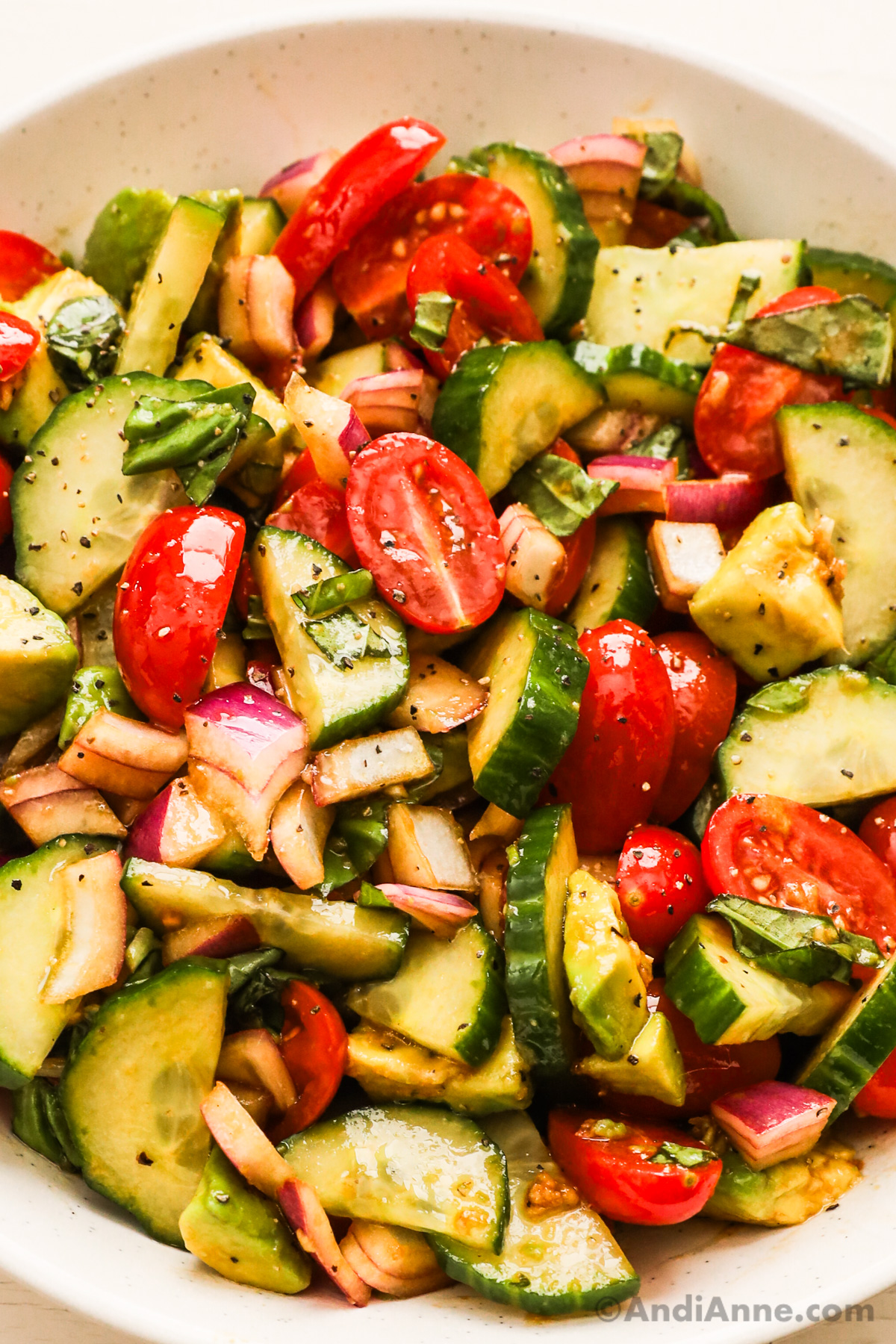 Close up of chopped cucumber, tomato, onion, avocado and basil in a salad.
