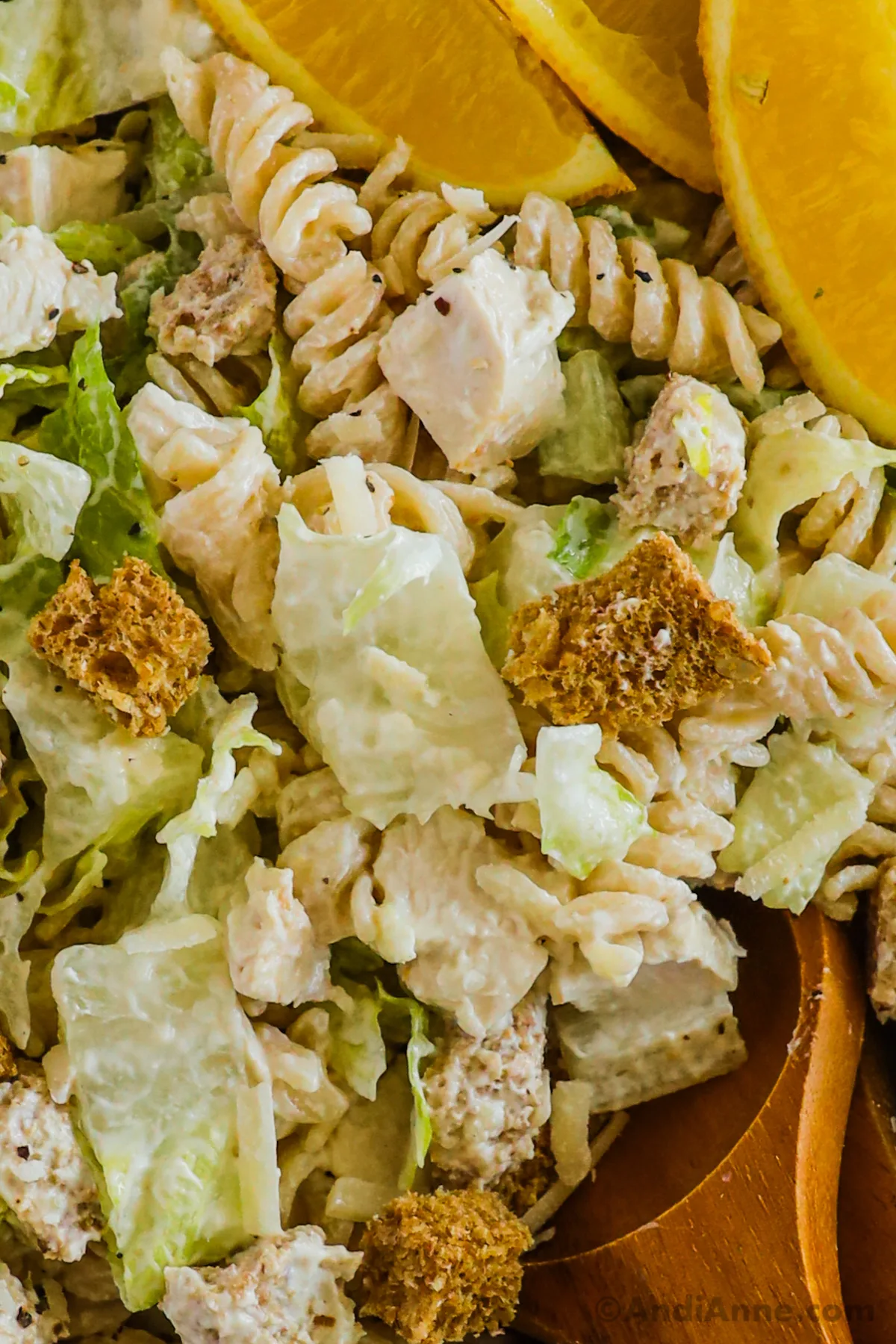 Close up of chopped chicken, rotini pasta, croutons and lettuce in a creamy pasta salad recipe.