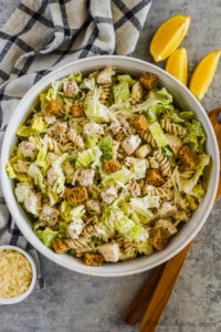 A bowl of chicken caesar pasta salad with lemon wedges, grated parmesan beside