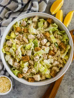 A bowl of chicken caesar pasta salad with lemon wedges, grated parmesan beside