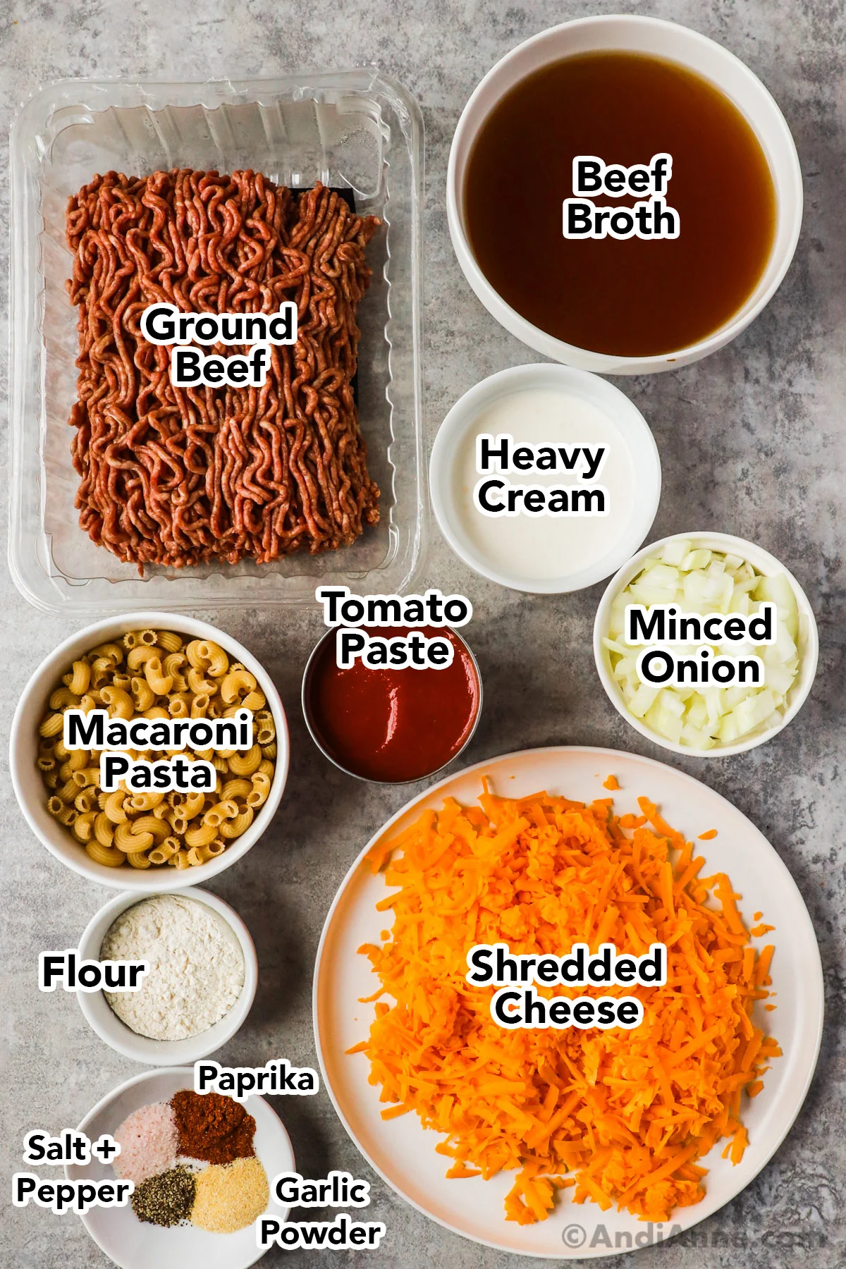 Recipe ingredients in containers including raw ground beef, broth, heavy cream, minced onion, tomato paste, macaroni pasta, shredded cheese, spices and flour