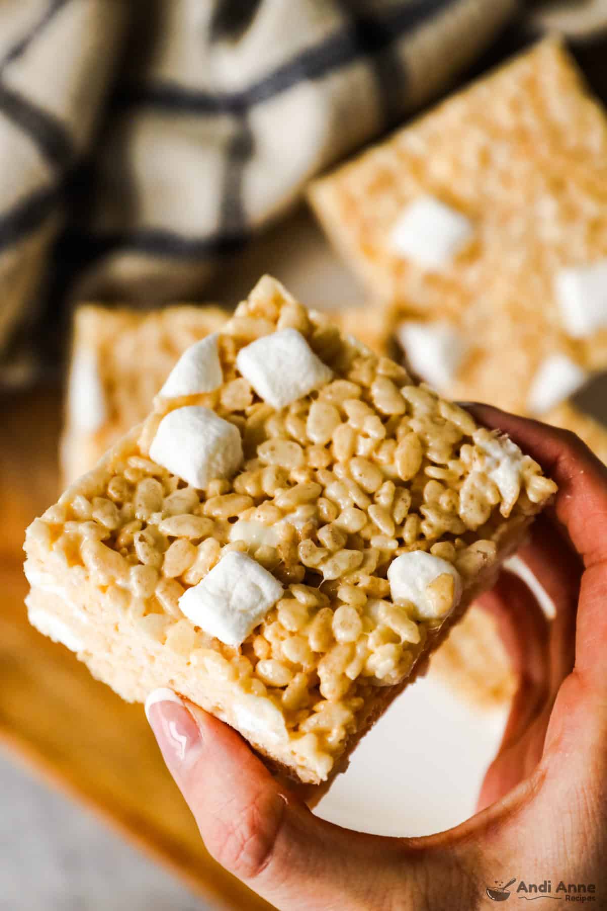 hand holidng a rice krispie square topped with extra marshmallows