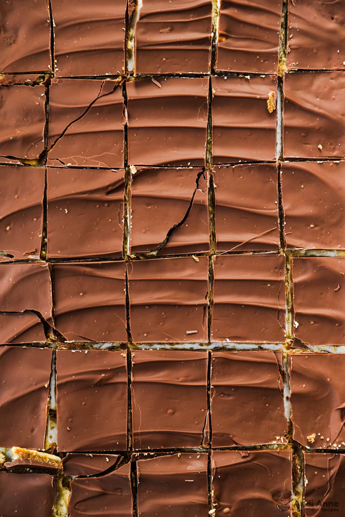 Cut squares of Christmas crack saltine toffee candy arranged on a table with the toffee and chocolate layers visible.