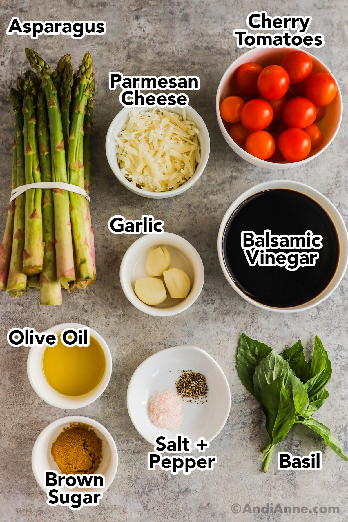 Recipe ingredients including bundle of asparagus, bowl of shredded parmesan, bowl of cherry tomatoes, bowls of balsamic vinegar, olive oil, brown sugar, garlic cloves and basil leaves