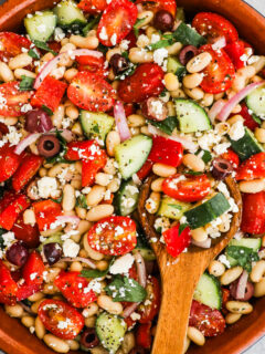 A large bowl of mediterranean white bean salad with a wood spoon