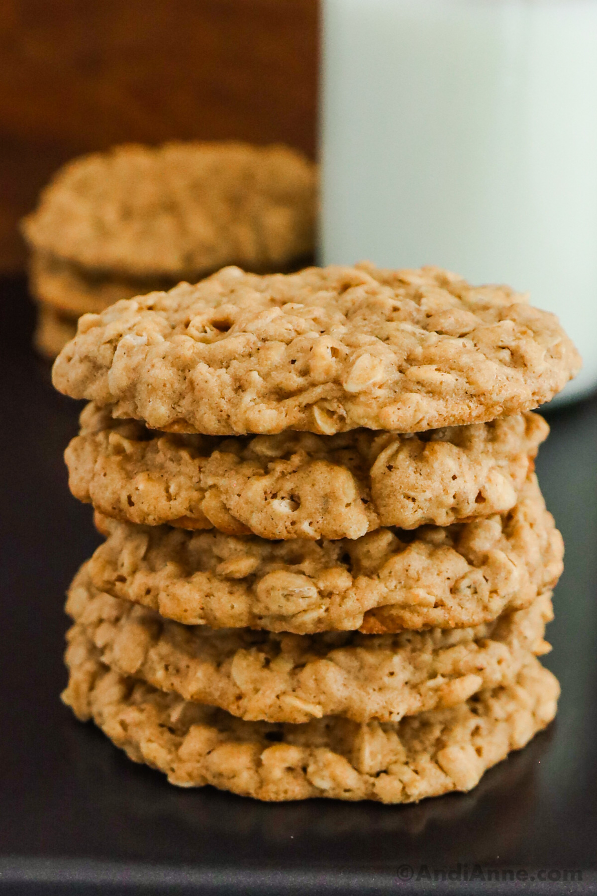 stack of oatmeal cookies with cup of milk in background