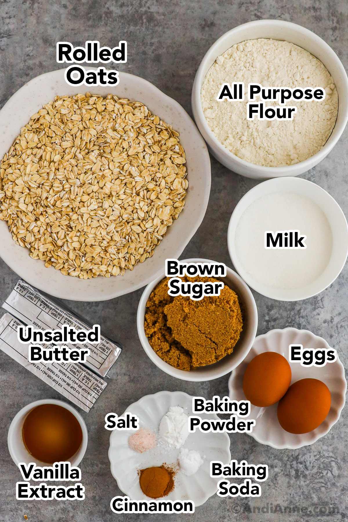 Recipe ingredients in bowls including rolled oats, flour, milk, brown sugar, eggs, baking powder, vanilla extract and sticks of butter