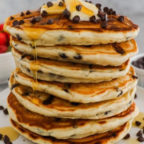 A stack of chocolate chip pancakes topped with butter, maple syrup and more mini chocolate chips