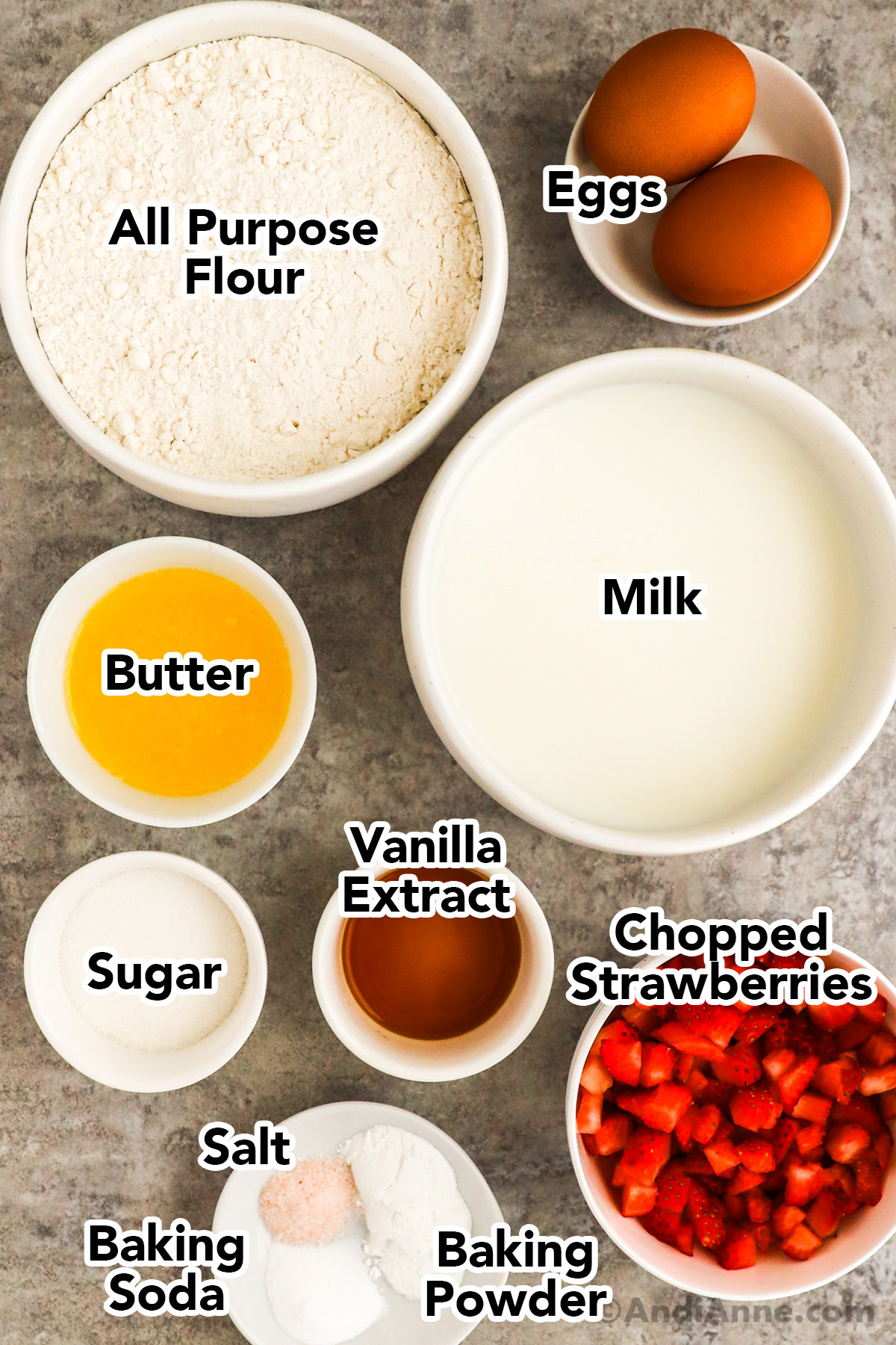 Recipe ingredients in bowls including flour, egg, milk, butter, vanilla extract, sugar, chopped strawberries and baking powder