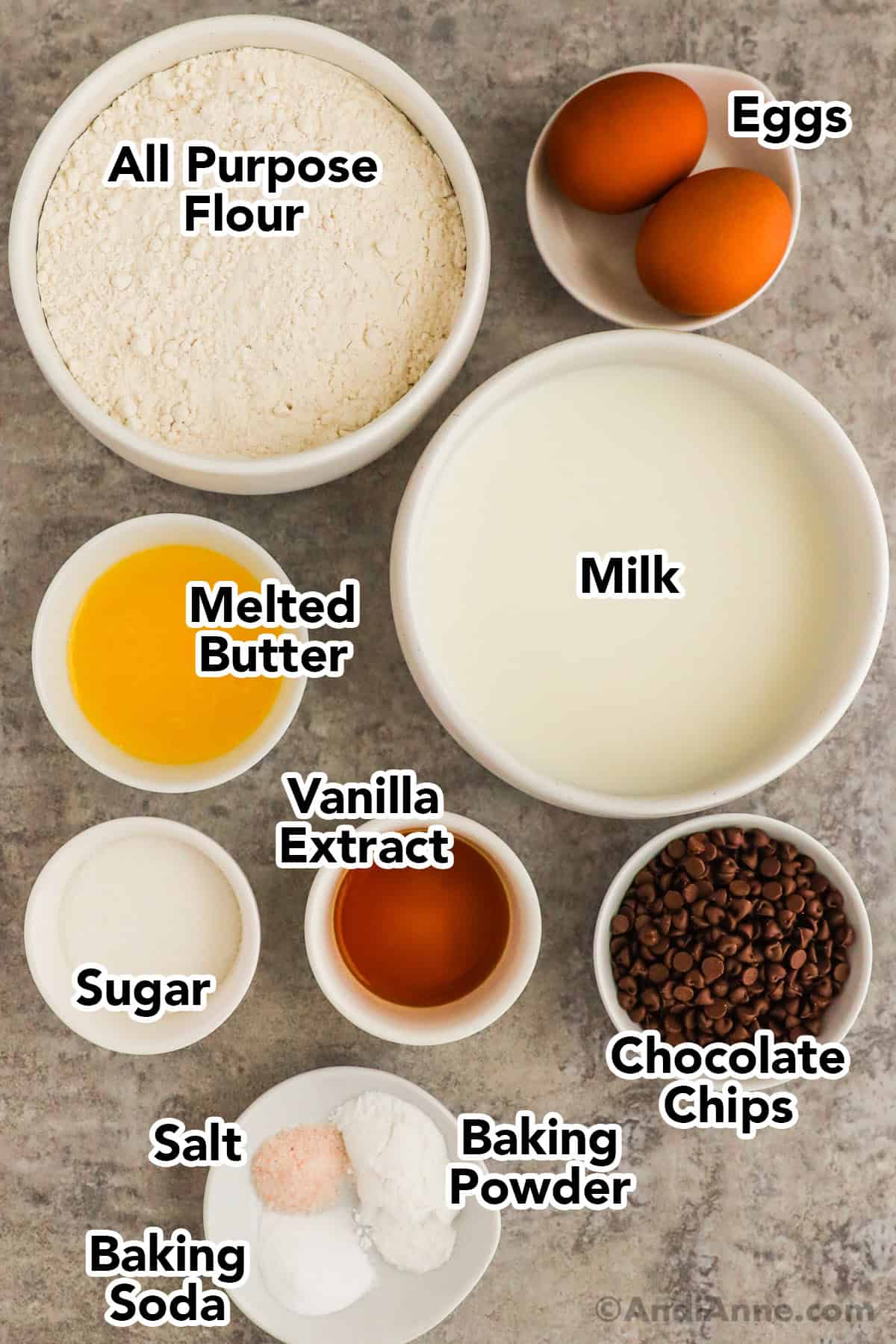 Recipe ingredients in bowls including flour, eggs, milk, melted butter, sugar, vanilla extract and chocolate chips