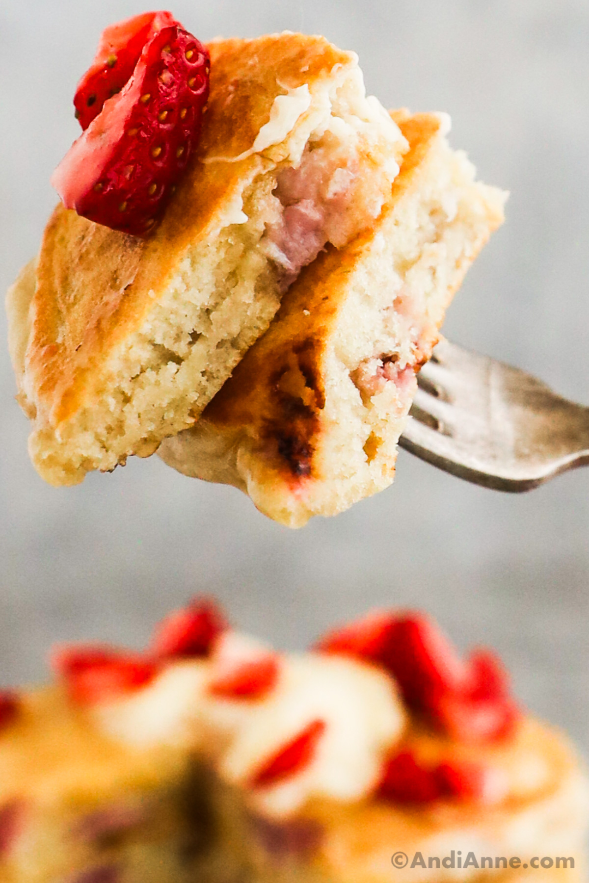 A fork holding a bite of pancakes with strawberry