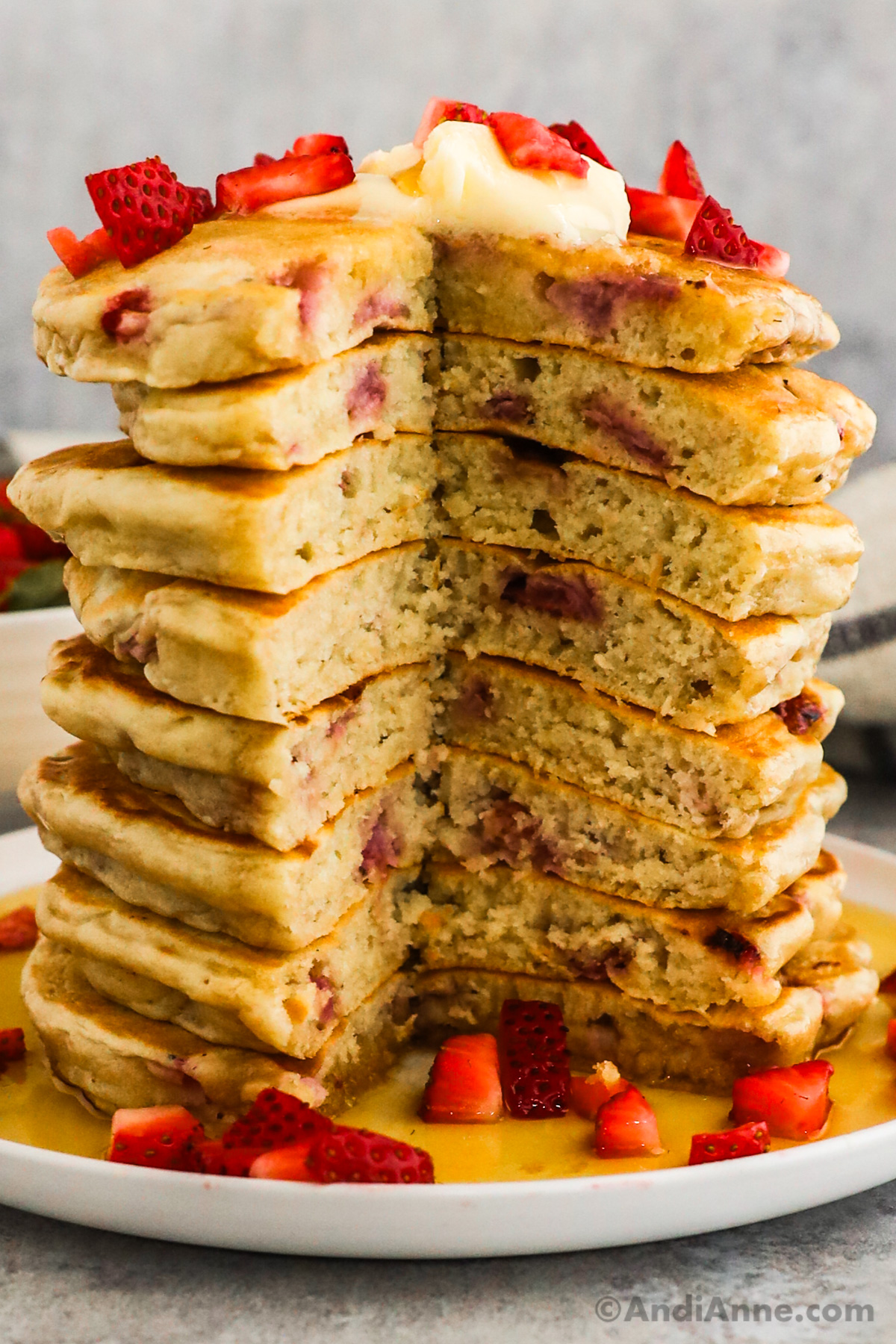 A stack of strawberry pancakes with a slice cut down through all of them to see the light and fluffy inside.