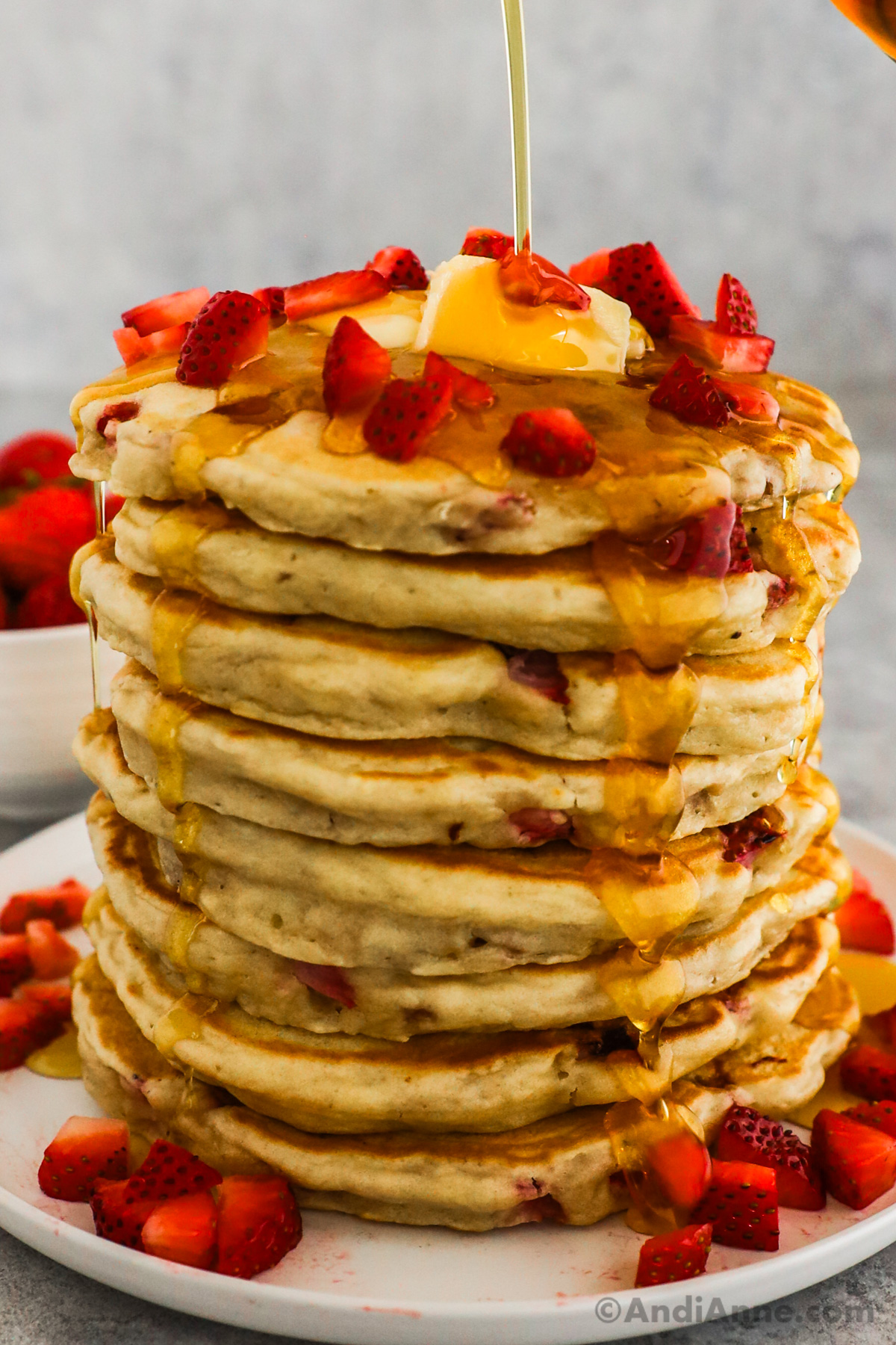 A stack of strawberry pancakes, topped with butter, more strawberries and drizzled with maple syrup