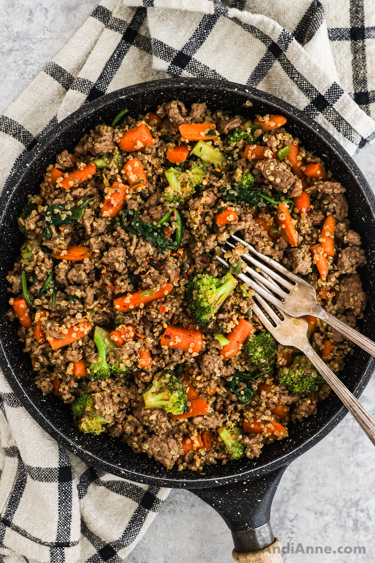 A frying pan with quinoa, ground beef, carrots and broccoli stir fry and two forks