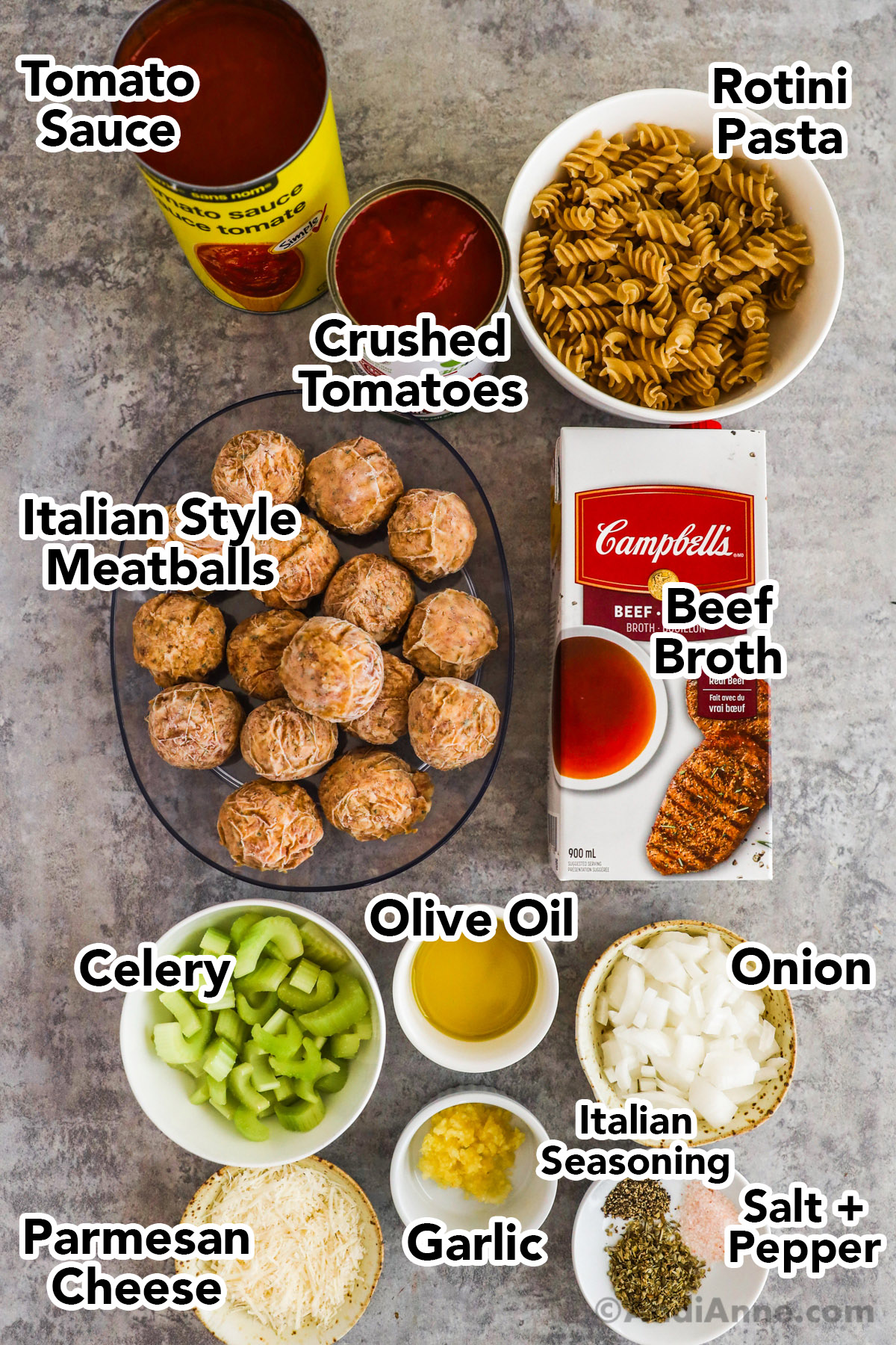 Recipe ingredients including canned tomato sauce, rotini pasta, beef broth carton, frozen meatballs, bowls of olive oil, chopped celery, chopped onion, grated parmesan cheese and spices