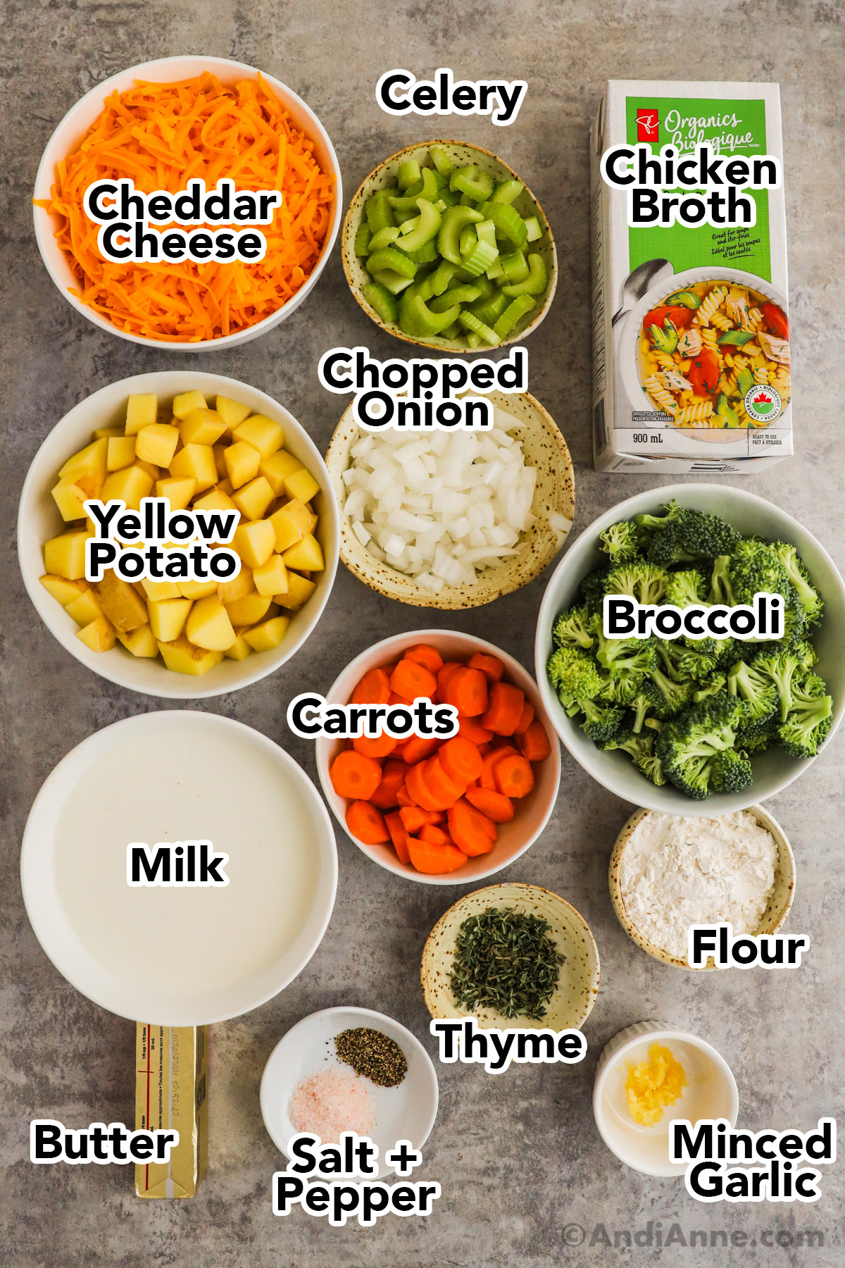 Recipe ingredients in bowls including cheddar cheese, celery, chopped potatoes, onions, broccoli, carrots, milk, butter, minced garlic and fresh thyme