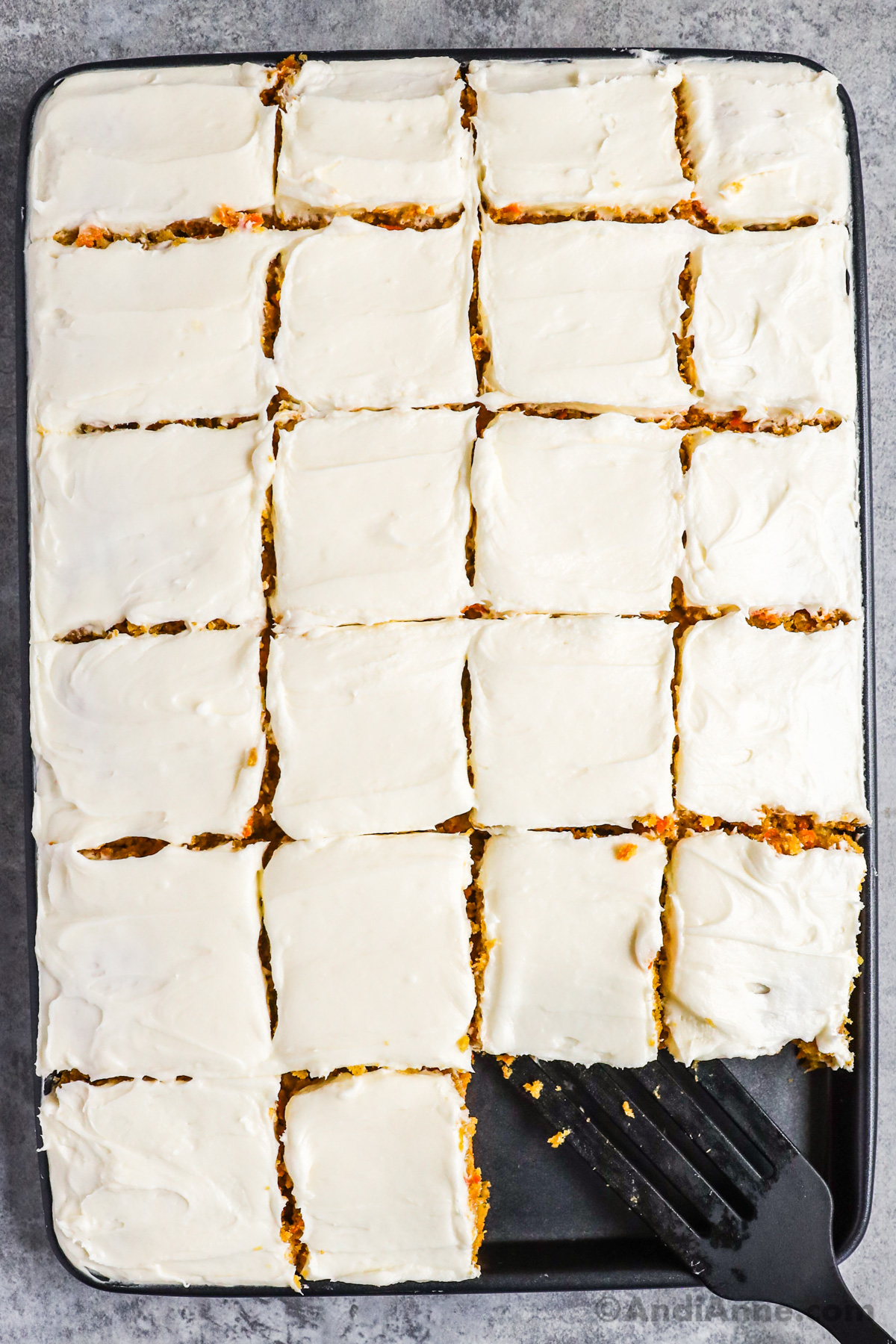 Sliced carrot cake covered in cream cheese frosting cooked in a baking sheet.