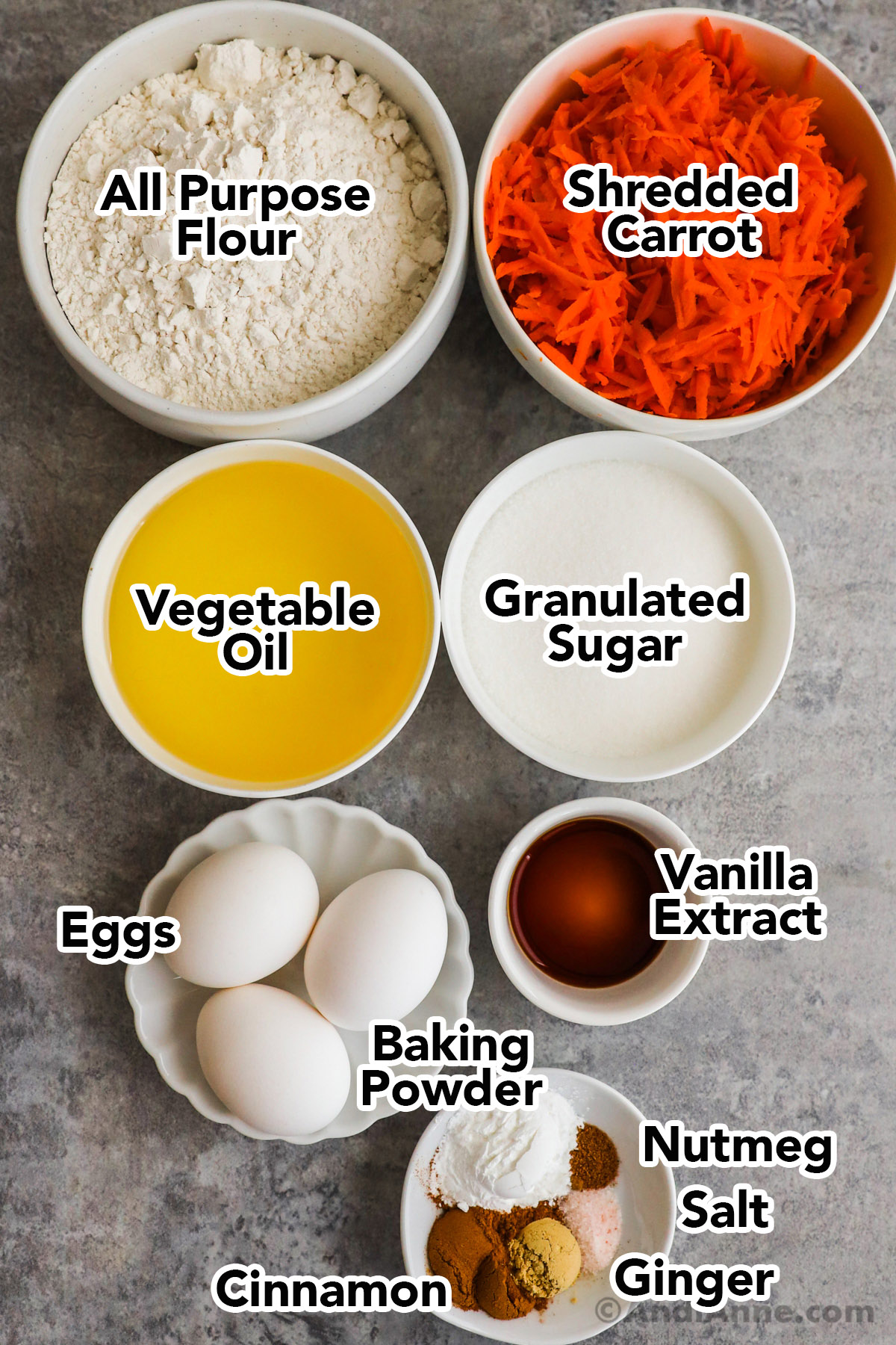 Recipe ingredients in bowls including flour, shredded carrots, vegetable oil, granulated sugar, eggs, vanilla extract and spices.