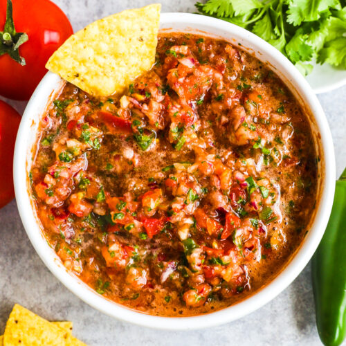 A bowl of homemade salsa with tomatoes, cilantro, chips and jalapeno beside.