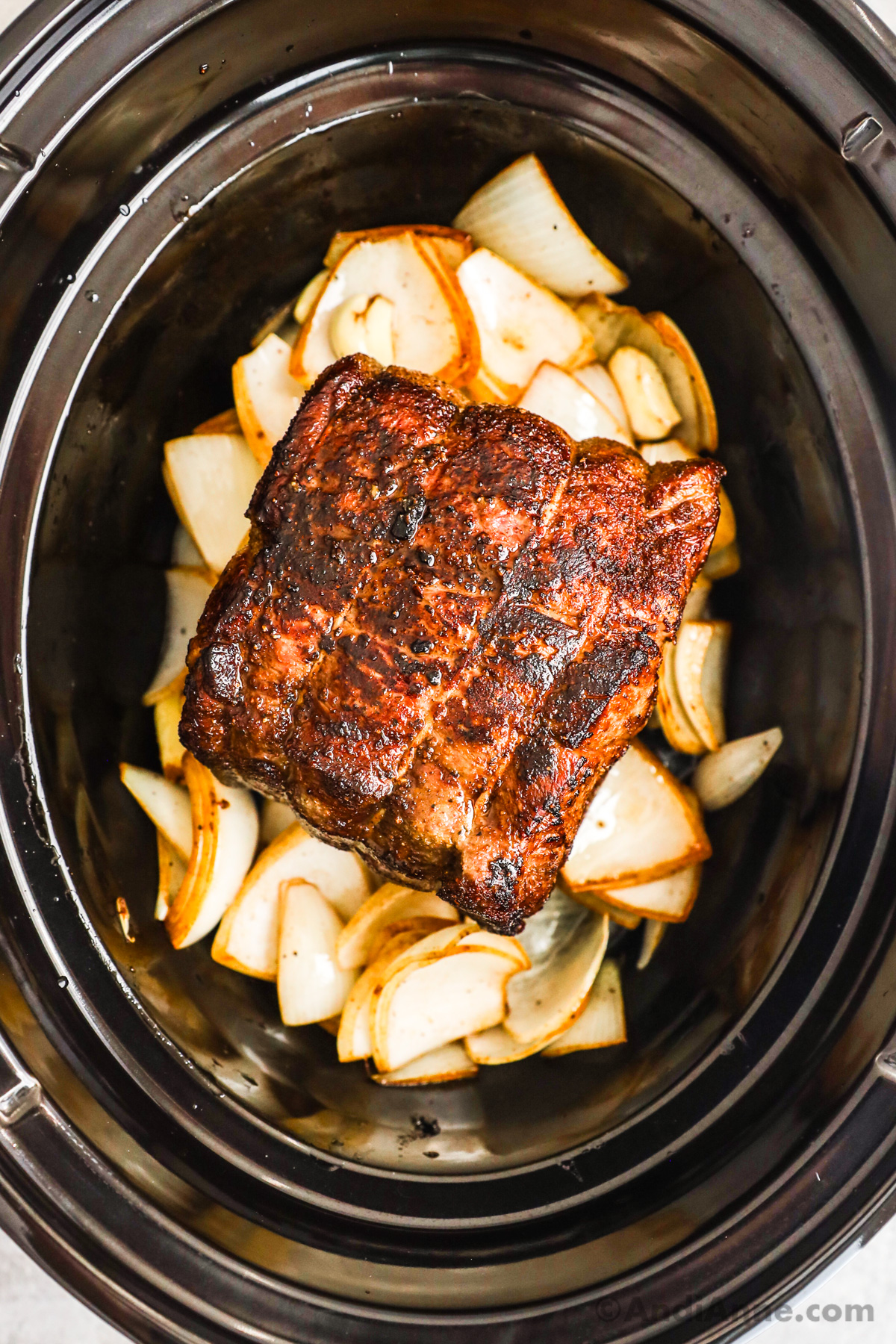 A slow cooker with cooked onion chunks and seared beef roast.