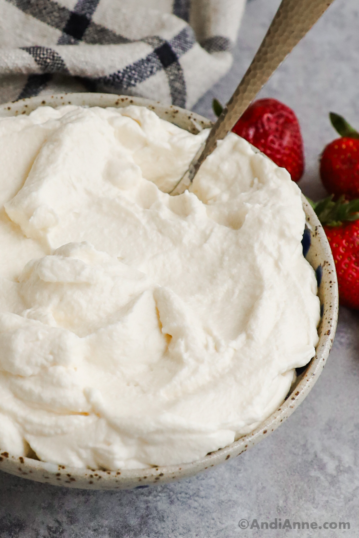 A bowl of whipped cream with a spoon, and a few fresh strawberries on the side.