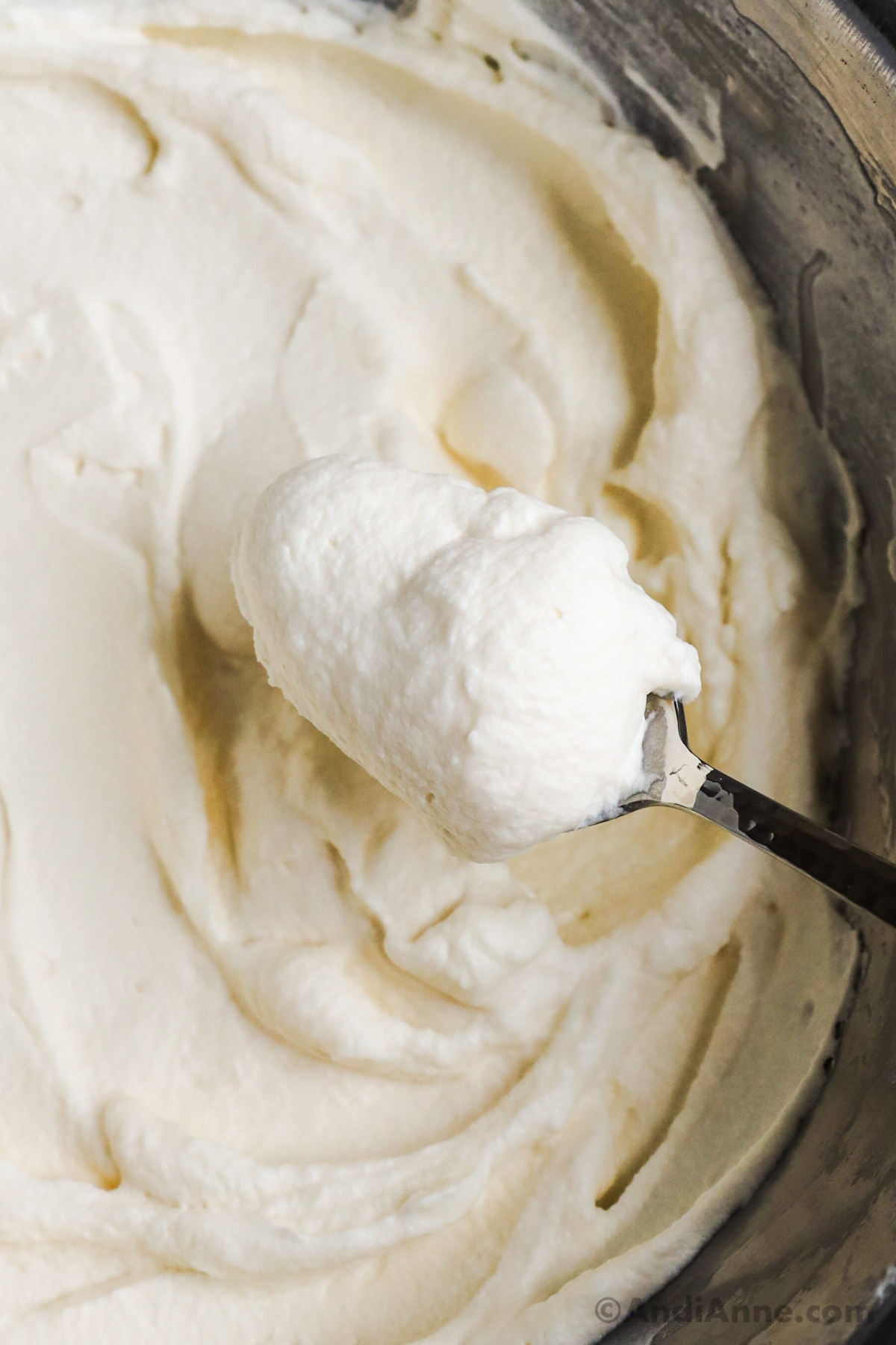 Close up of a spoon scooping whipped cream from a bowl.