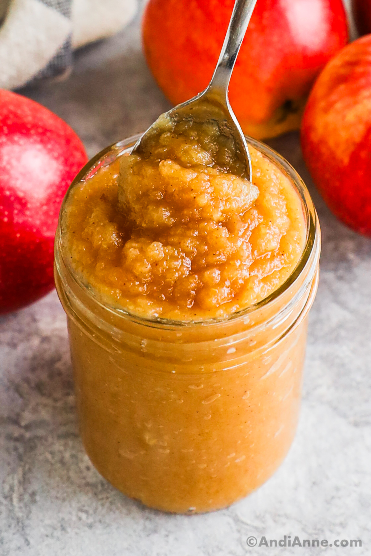 Mason jar of apple sauce with a spoon and apples in the background.